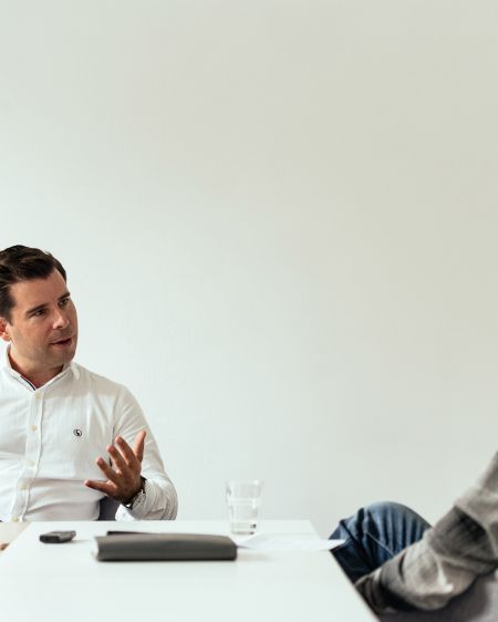 Felix Haas sitzt am Tisch gegenüber von Stefan Ruzas, der ihm aufmerksam zuhört