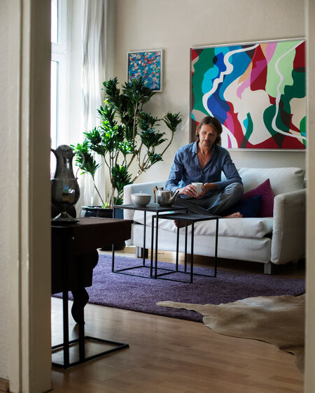 Markus Tenbusch sitzt mit einem Kaffee in einem LAB-Becher von KPM Berlin auf dem Sofa in seiner Wohnung.