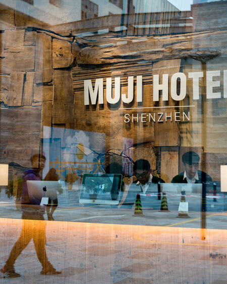 Rezeption des Muji Hotel in Shenzen durch Fensterscheibe fotografiert, in der sich Straße mit Passanten spiegelt