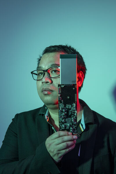 Blau belichtetes Porträtfoto des chinesischen Investors Robin Wu, der Elektroplatine hält