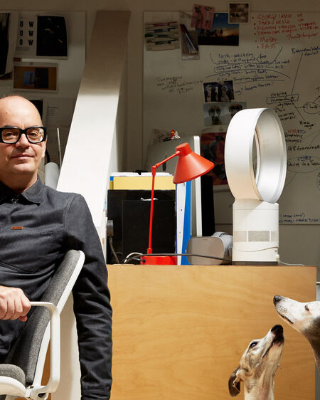 Brendan Walker sitzt auf Stuhl in seinem Büro, während zwei Windhunde neben ihm auf dem Boden liegen