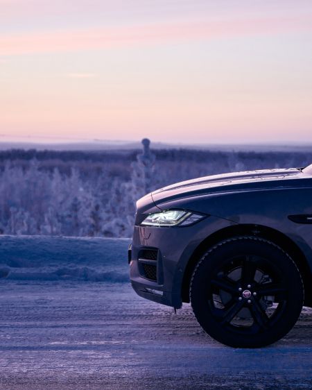 Jaguar F-PACE auf einer verschneiten Straße bei Sonnenuntergang und lila gefärbtem Himmel