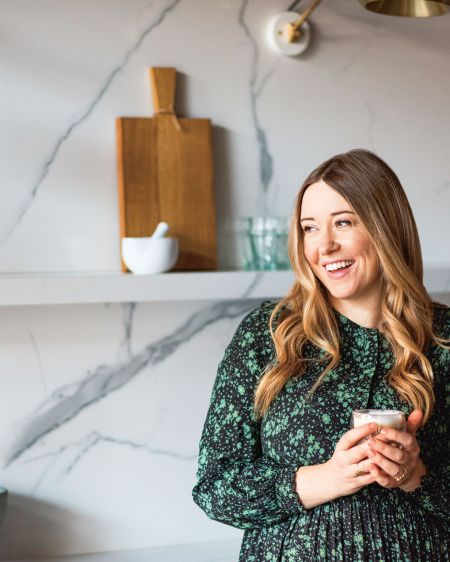 Starköchin Anna Jones lehnt an ihrer Küchenzeile mit einem Becher in der Hand