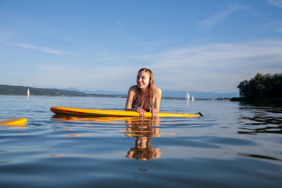 E-Boot fahren auf dem Ammersee für SeeMagazin 2021 Junge Frau stützt sich auf SUP Board im Wasser