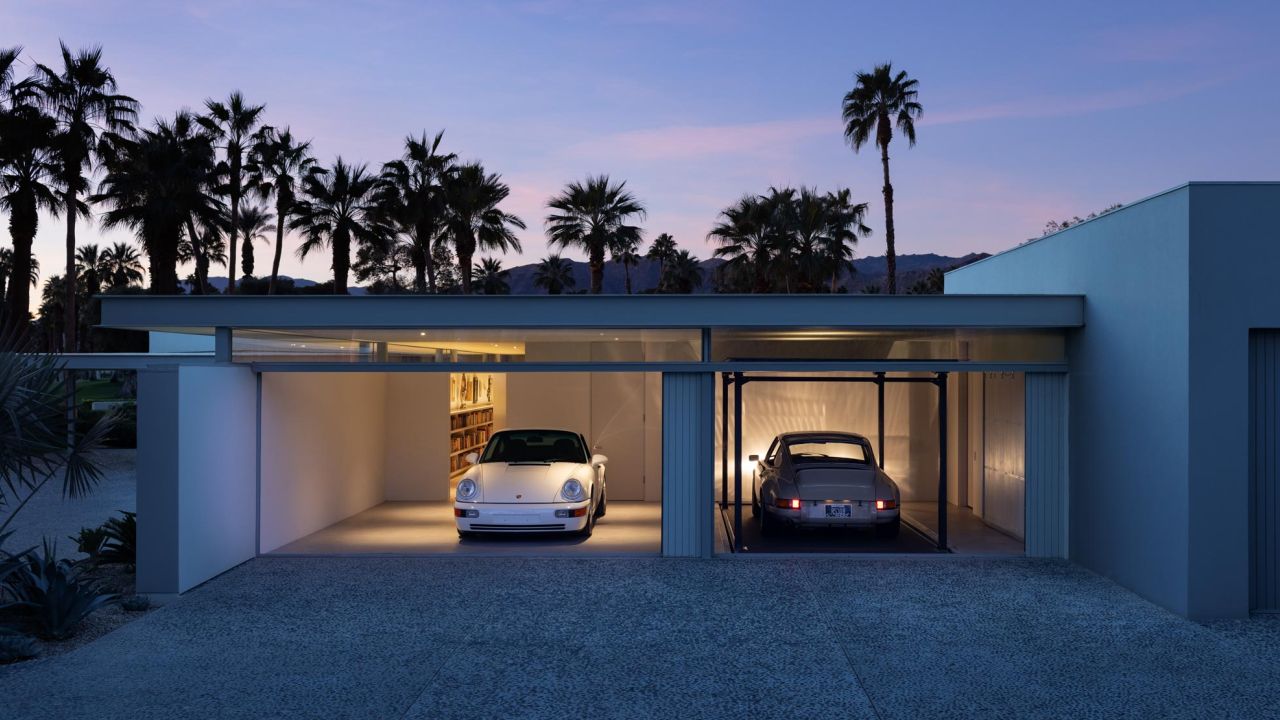 Modernes Garagenhaus bei Abenddämmerung mit zwei klassischen Porsches und Palmen im Vordergrund